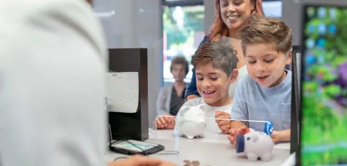 Dwójka dzieci z mamą wpłaca w banku pieniądze na konto oszczędnościowe
