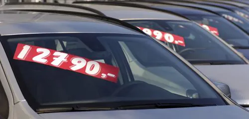 Samochody wystawione na sprzedaż z naklejkami na szybach, które przedstawiają ceny.