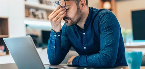 Załamany mężczyzna siedzący przed laptopem, próbujący zaciągnąć kredyt z komornikiem online