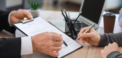 Zbliżenie na kobietę podpisującą dokumenty we wskazanym miejscu.