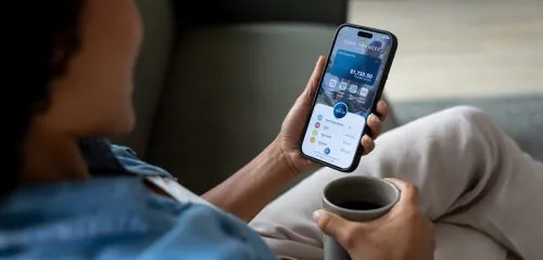 Zbliżenie na kobietę siedzącą z kawą i sprawdzającą na smartfonie saldo konta bankowego.