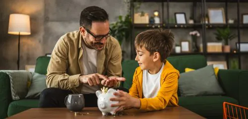 Ojciec wrzuca z synem pieniądze do świnki skarbonki i uczy go oszczędności