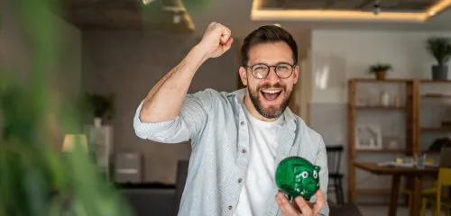 Mężczyzna w średnim wieku z zieloną świnką skarbonką w dłoni.