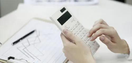 Kobieta wylicza coś na kalkulatorze, a przed nią leży notes z wykresem giełdowym