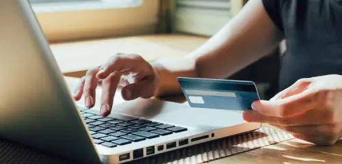 mężczyzna siedzący przy laptopie korzystający z karty kredytowej z debetem