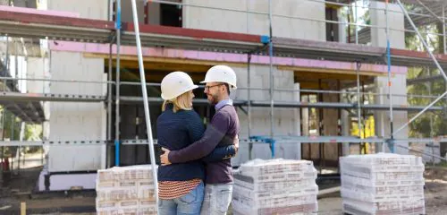 Małżeństwo w białych kaskach sprawdzające postępy na budowie domu jednorodzinnego.