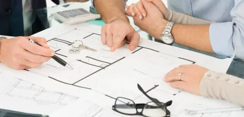 Trzy osoby siedzą przy projekcie i zastanawiają się co bardziej się opłaca dom czy mieszkanie