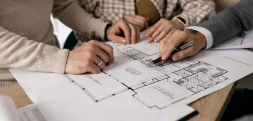ludzie siedzący nad projektem budowlanym zastanawiający się co się bardziej opłaca, kupić mieszkanie czy wybodować dom