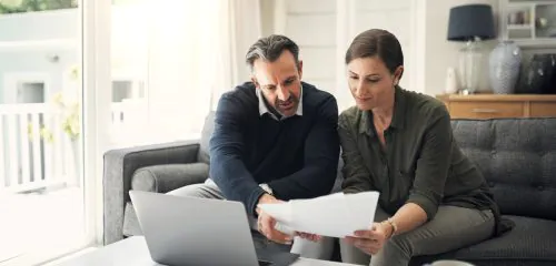 Małżeństwo w średnim wieku siedzące w salonie przed dokumentami i sprawdzające, gdzie najłatwiej dostać kredyt hipoteczny.