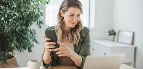 kobieta siedząca przed laptopem i sprawdzająca w smartfonie przelew do Santander Bank Polska