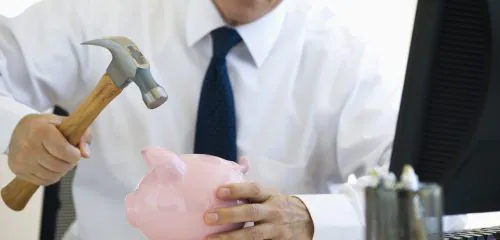 Biznesmen zamierzający rozbić młotkiem różową świnkę skarbonkę