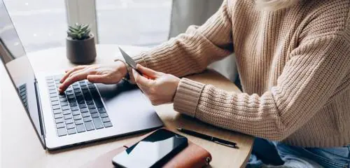 kobieta w beżowym swetrze sprawdzająca na laptopie, jak aktywować nową kartę w PKO BP