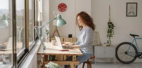 rudowłosa kobieta siedząca przy biurku i sprawdzająca na laptopie, jak zamknąć konto w Banku Pekao