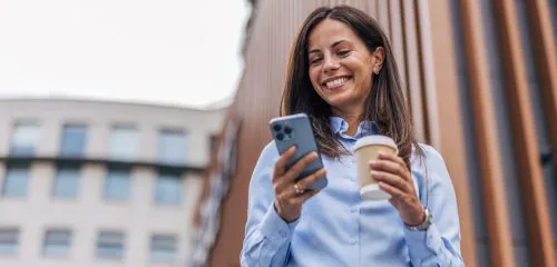Zadowolona, młoda kobieta w błękitnej koszuli odbierająca na smartfonie czek BLIK