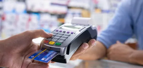 Zbliżenie na męską dłoń i terminal w trakcie płatności kartą w sklepie.