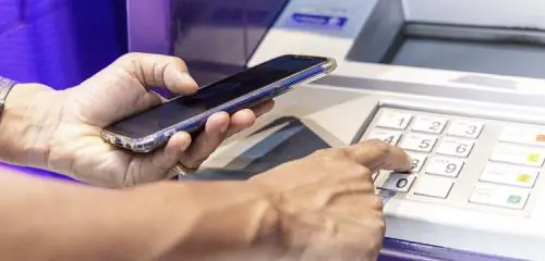 mężczyzna trzymający w dłoni smatrfon sprawdza, jak działa wypłata BLIK z bankomatu