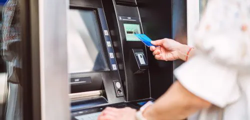 Zbliżenie na kobietę, która stoi z kartą przy bankomacie i sprawdza, jak wypłacić pieniądze