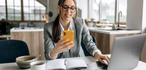 młoda kobieta siedząca przy biurku i sprawdzająca na smartfonie ranking pożyczek 1800 zł