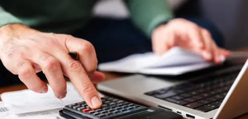 Mężczyzna liczy na kalkulatorze jak szybko spłacić kredyt