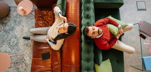 Mężczyzna i kobieta pokłóceni siedzą na dwóch kanapach tyłem do siebie.