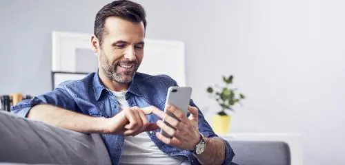 mężczyzna siedzący na sofie ze smartfonem i sprawdzający, co to jest lokata mobilna