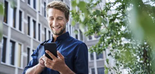 Zadowolony mężczyzna w niebieskiej koszuli zakładający przez smartfon lokatę mobilną.