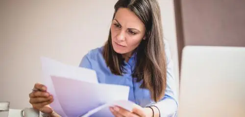kobieta w niebieskiej koszuli siedząca przy biurku i sprawdzająca w umowie, czy możliwa jest nadpłata kredytu hipotecznego w BNP Paribas