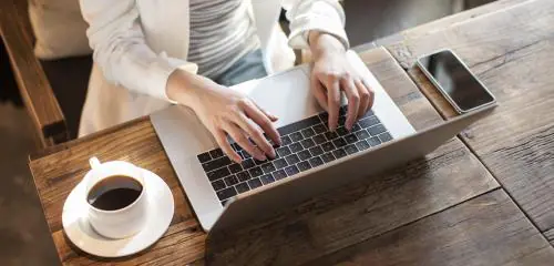 kobieta siedząca przy laptopie z kawą i zlecająca przelew z Nest Banku