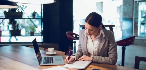 kobieta siedząca przy biurku i wypełniająca wniosek o kredyt konsolidacyjny dla firm.