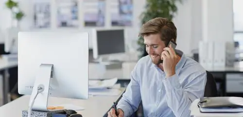 mężczyzna siedzący w biurze przed komputerem sprawdzający przez telefon warunki lokaty negocjowanej