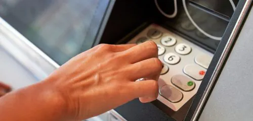 Mężczyzna wypłaca pieniądze z bankomatu