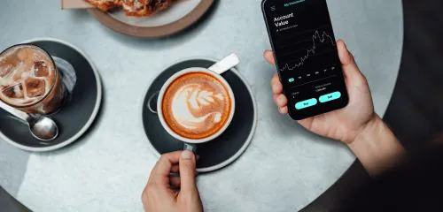 Kobieta siedząca w kawiarni i sprawdzająca na ekranie smartfonu, jaki dochód pasywny generuje jej inwestycja w akcje.