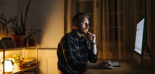 Młody mężczyzna siedzący nocą przed komputerem i sprawdzający, jak pracuje lokata overnight