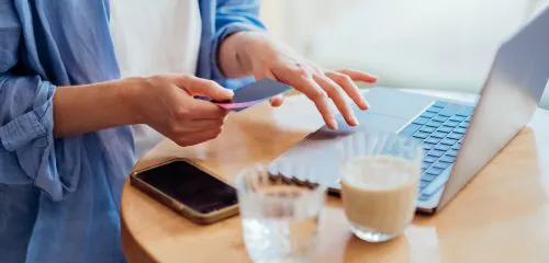 Zbliżenie na dłonie kobiety i laptop podczas wykonywania płatności kartą w internecie.