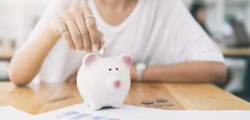 kobieta wrzucająca monety do świnki skarbonki