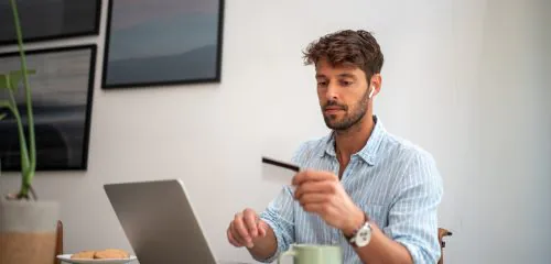 Młody mężczyzna siedzący przed laptopem i sprawdzający datę ważności karty.