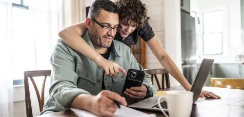 Mężczyzna pracuje przy komputerze, a kobieta pokazuje mu coś w telefonie