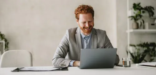 Zadowolony mężczyzna siedzący przed laptopem i sprawdzający najlepsze lokaty bankowe na 12 miesięcy.