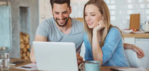 Zadowolone, młode małżeństwo sprawdzające na laptopie najlepsze lokaty bankowe na 12 miesięcy w rankingu online