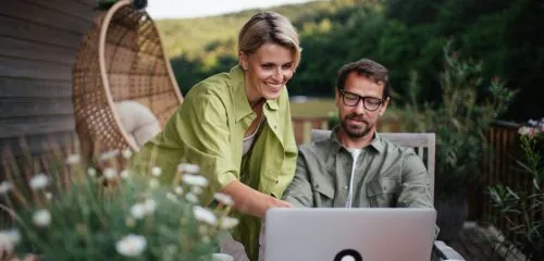 Para małżonków w sielskiej scenerii sprawdza na laptopie najlepsze lokaty na 6 miesięcy w lipcu 2025 roku