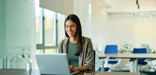Zadowolona kobieta siedząca w biurze i porównująca na laptopie najlepsze lokaty bankowe na 12 miesięcy