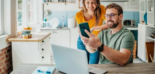 Młode małżeństwo przy stole z laptopem i smartfonem sprawdzające najlepsze lokaty bankowe na 12 miesięcy w rankingu online