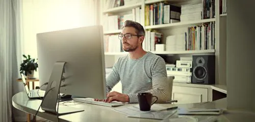 Mężczyzna siedzący przed dużym monitorem w domowym biurze i sprawdzający ranking lokat na 12 miesięcy