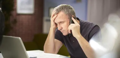 Wyraźnie zmartwiony mężczyzna siedzi przed laptopem i rozmawia przez telefon