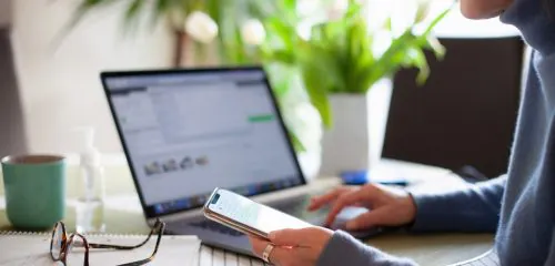 Kobieta siedząca przed laptopem, która sprawdza na smartfonie numer iban bnp paribas