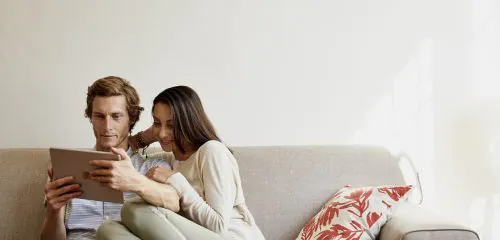 Młoda para siedząca na sofie z tabletem i przeglądająca ranking lokat bankowych na lipiec 2025