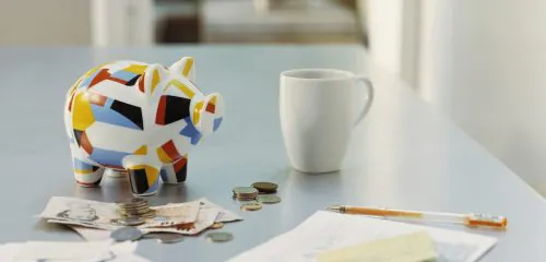 Kolorowa świnka skarbonka, banknoty, monety, kubek i dokumenty leżące na jasnym blacie