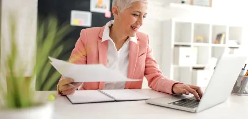 Starsza biznesmenka siedząca z umową przy biurku i sprawdzająca w usłudze bankowości elektronicznej kod SWIFT Pekao S.A.