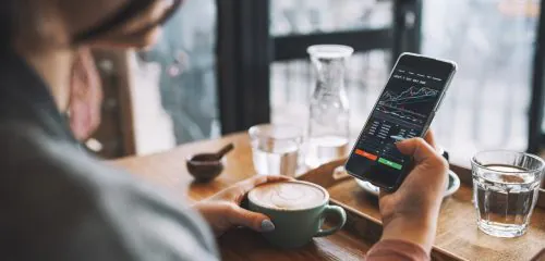 Kobieta siedząca przy stoliku w kawiarni i sprawdzająca na smartfonie, jak pracują jej oszczędności wpłacone na konto OKI