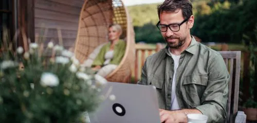 Mężczyzna siedzący z laptopem przed domem i sprawdzający ile kosztuje konsolidacja kredytu hipotecznego.